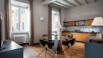 A modern dining area with a glass table, black chairs, and a kitchen in the background.