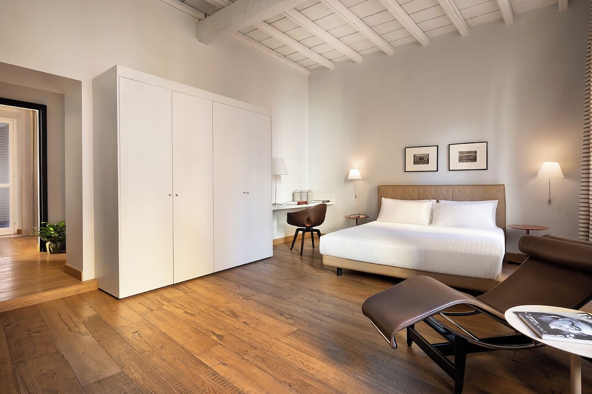A hotel room with a large bed, a desk, a chair, and a wardrobe.