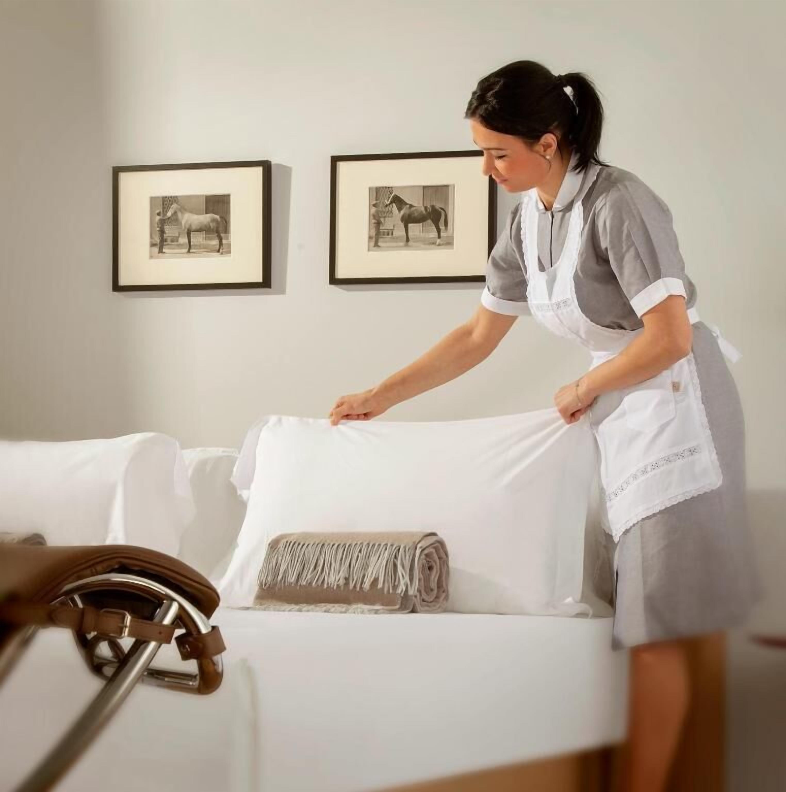 A person in a uniform cleaning a white sofa with a rolled-up blanket. Two framed pictures are on the wall behind.