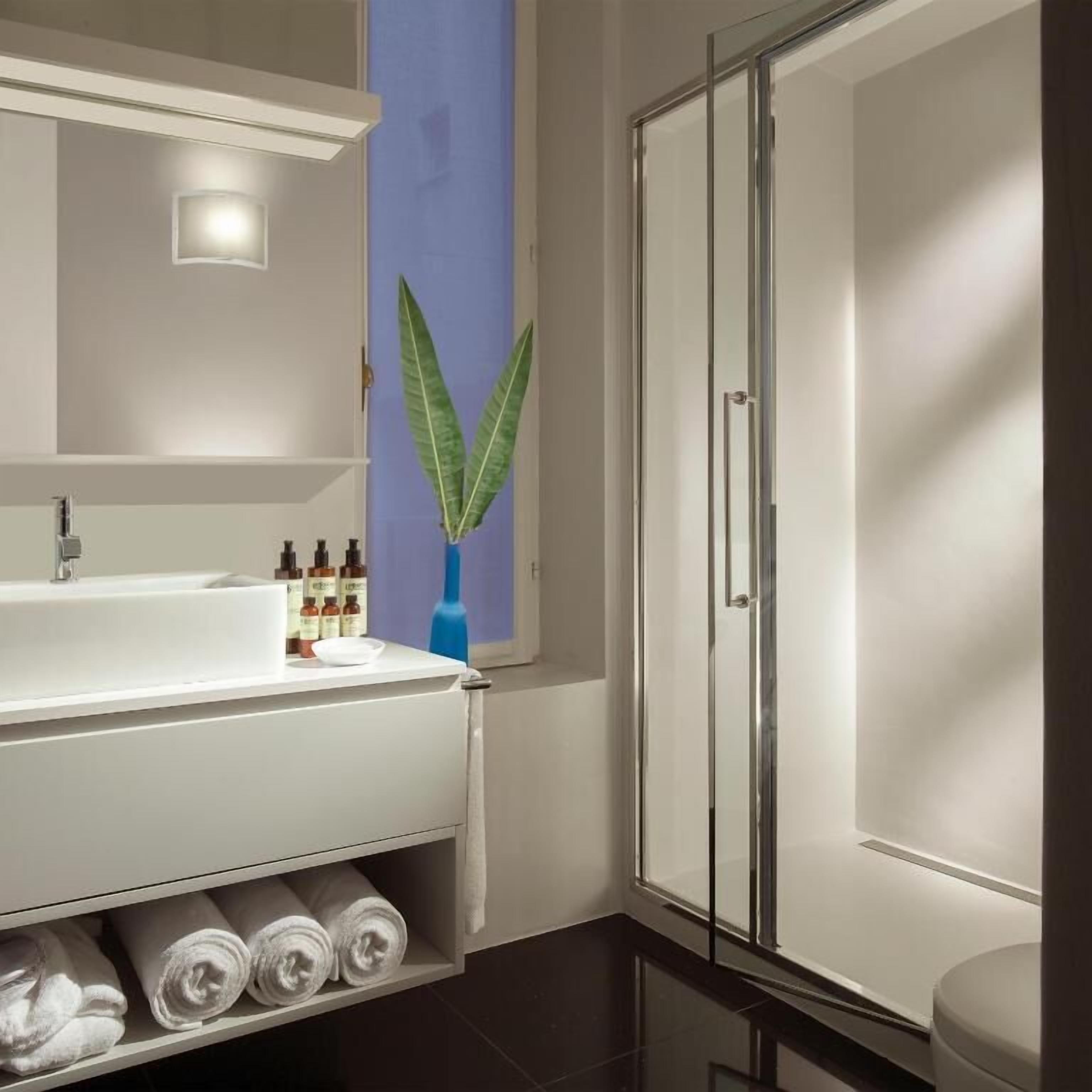 A modern bathroom with a white vanity, a glass shower enclosure, and a blue accent wall.