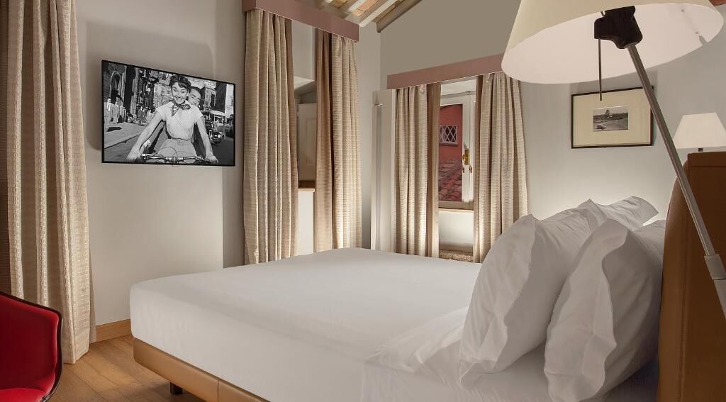 Une chambre d’hôtel avec un grand lit, un fauteuil rouge, un bureau, une lampe et un tableau encadré au mur.