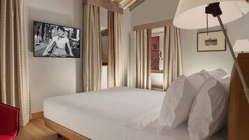 A hotel room with a large bed, a red chair, a desk, a lamp, and a framed picture on the wall.