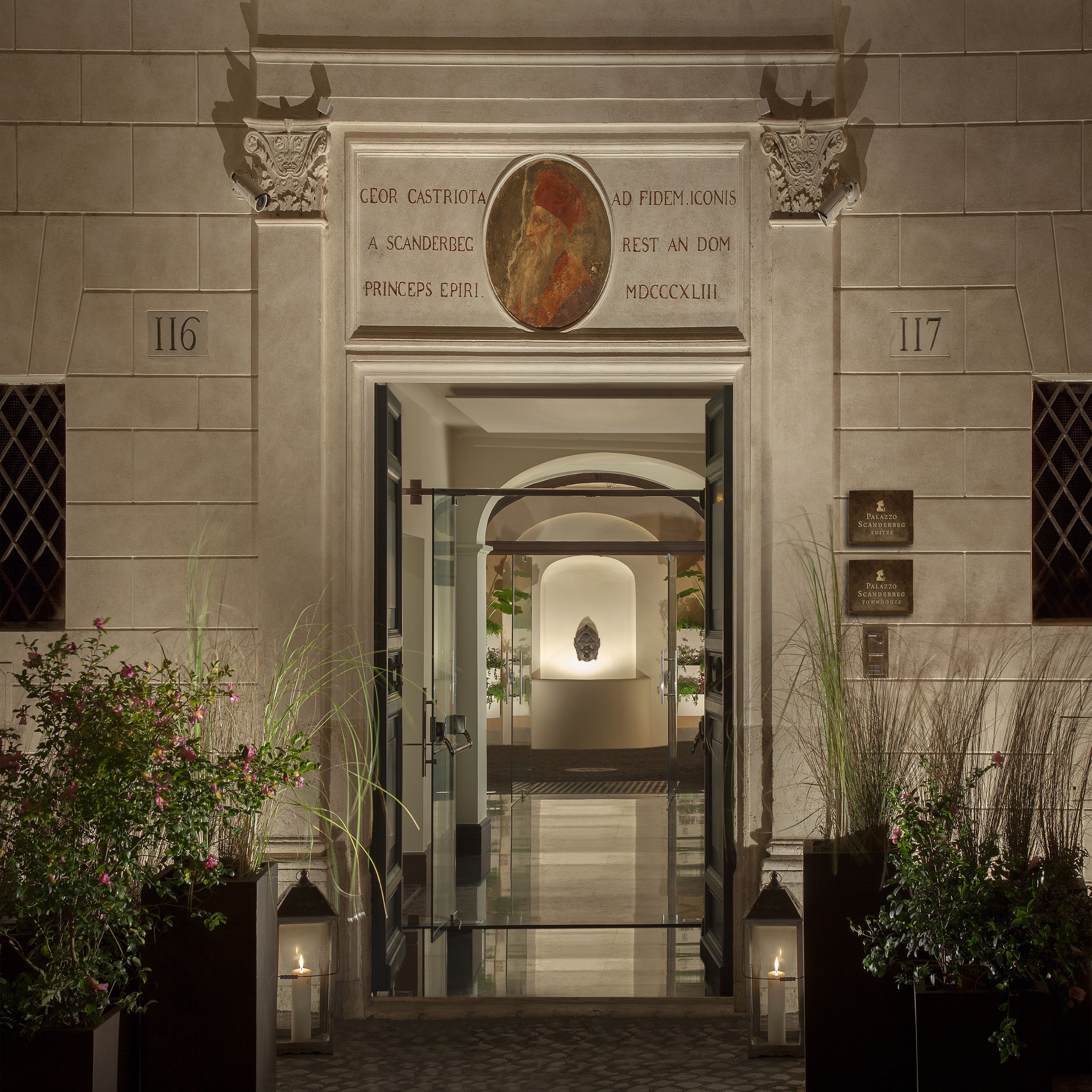 A building entrance with a plaque reading "Palazzo Scanderbeg Suites" and a number "117".