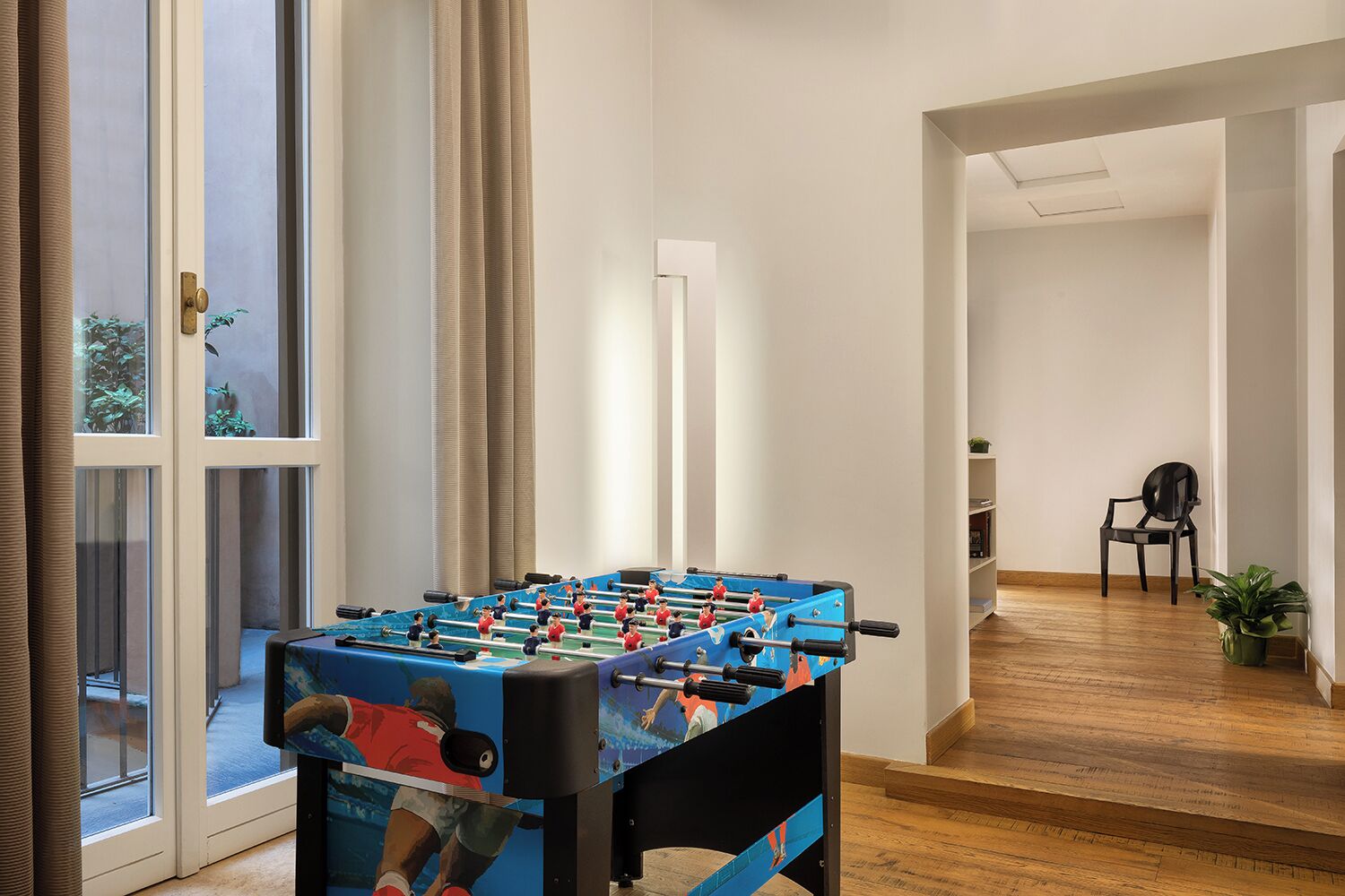 A room with a foosball table, a chair, and a potted plant.