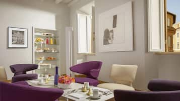 Un salon moderne avec des fauteuils violets et beiges, une table basse blanche et une bibliothèque contenant divers objets.