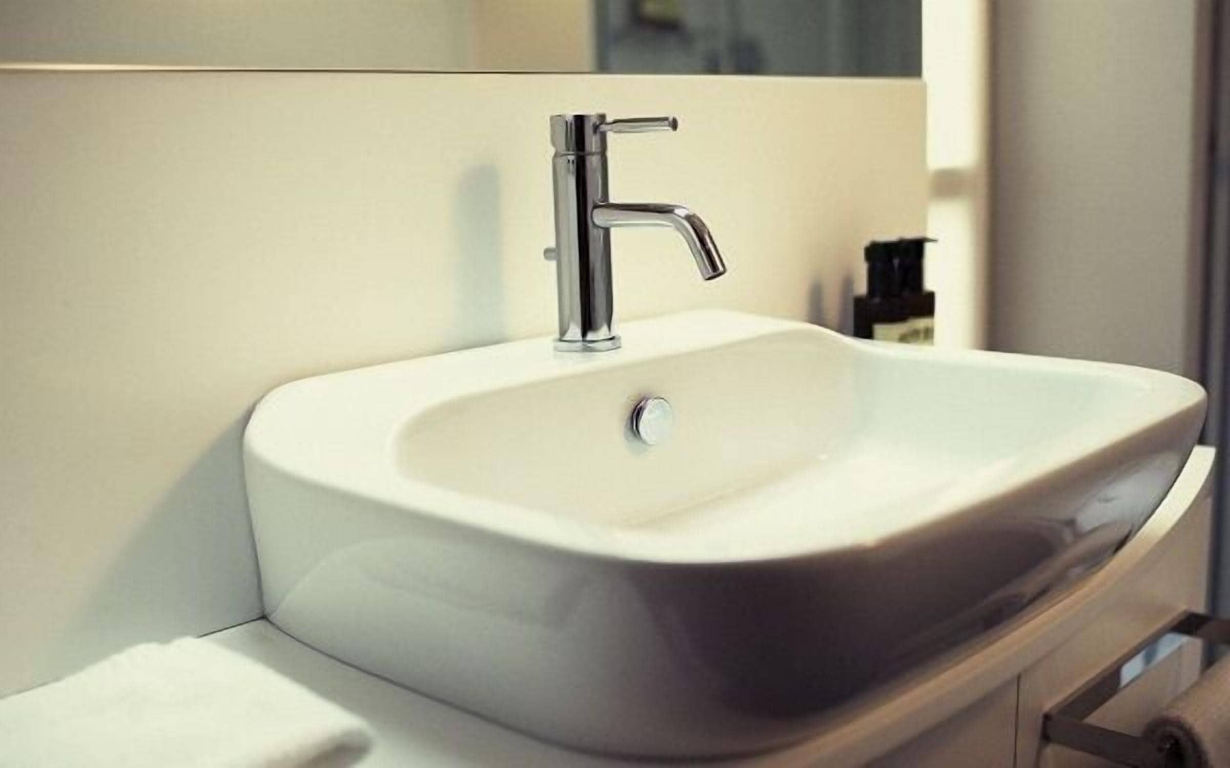 A modern bathroom sink with a chrome faucet, a white basin, and a mirror above it.