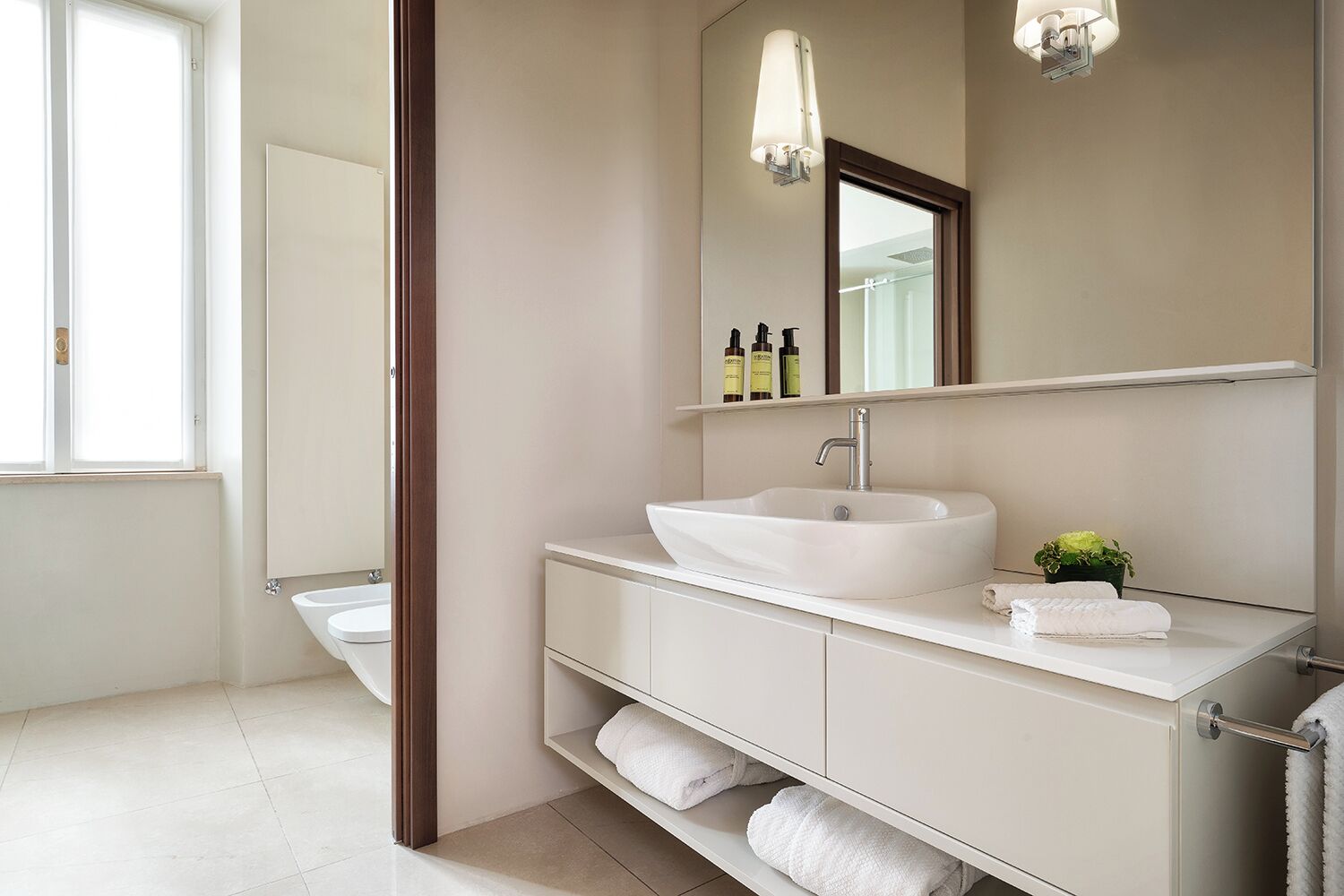 Un baño moderno con un lavamanos blanco, espejo y repisas con toallas.