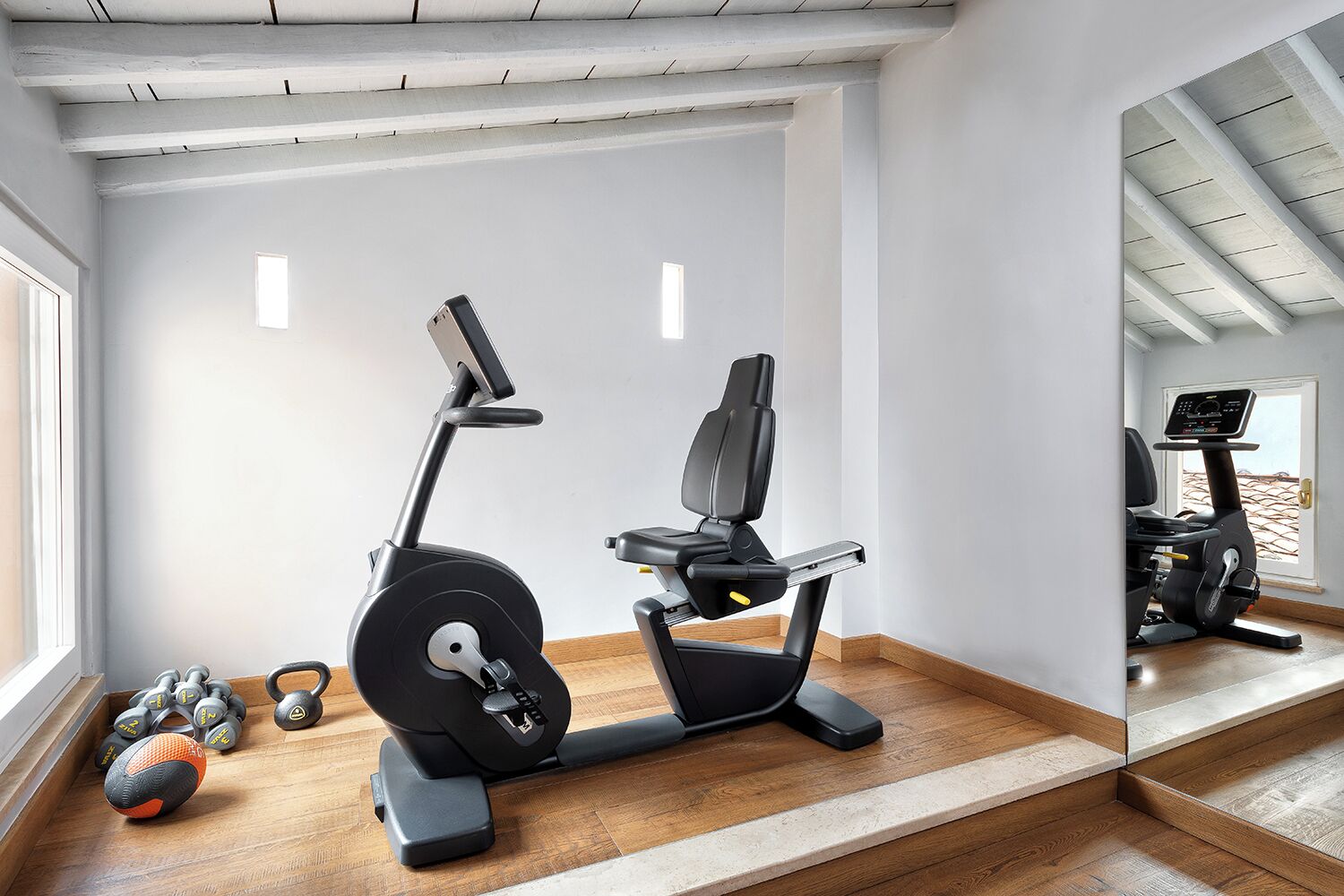 A home gym with an elliptical, a mirror, and a pair of dumbbells.