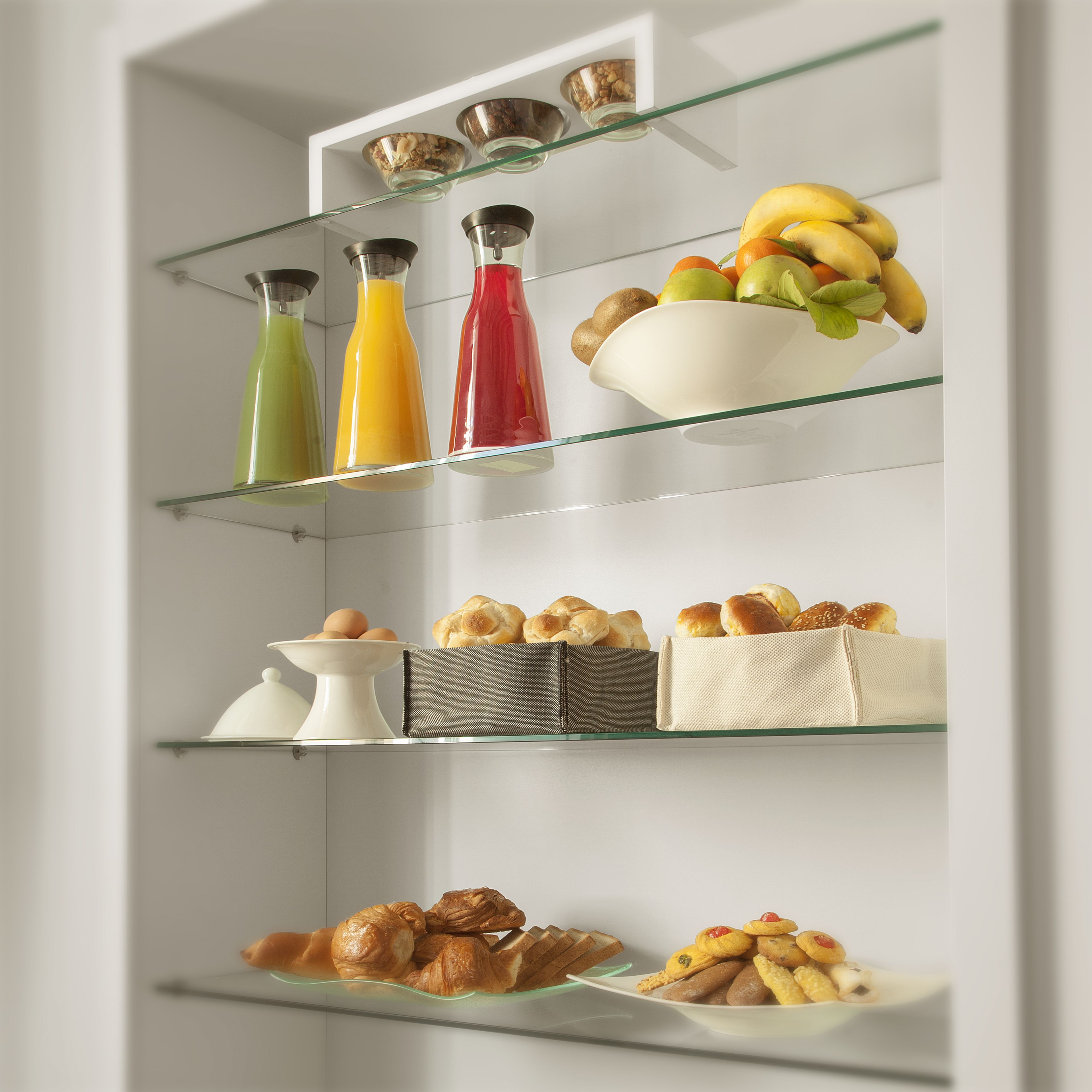 A kitchen with glass shelves displaying various food items and drinks.