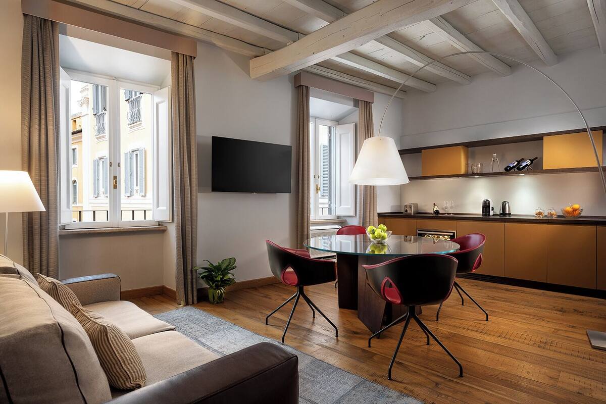 A modern living room with a glass dining table, red chairs, a sofa, and a TV.