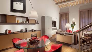 A modern living room with a glass dining table, red chairs, a sofa, and a staircase.