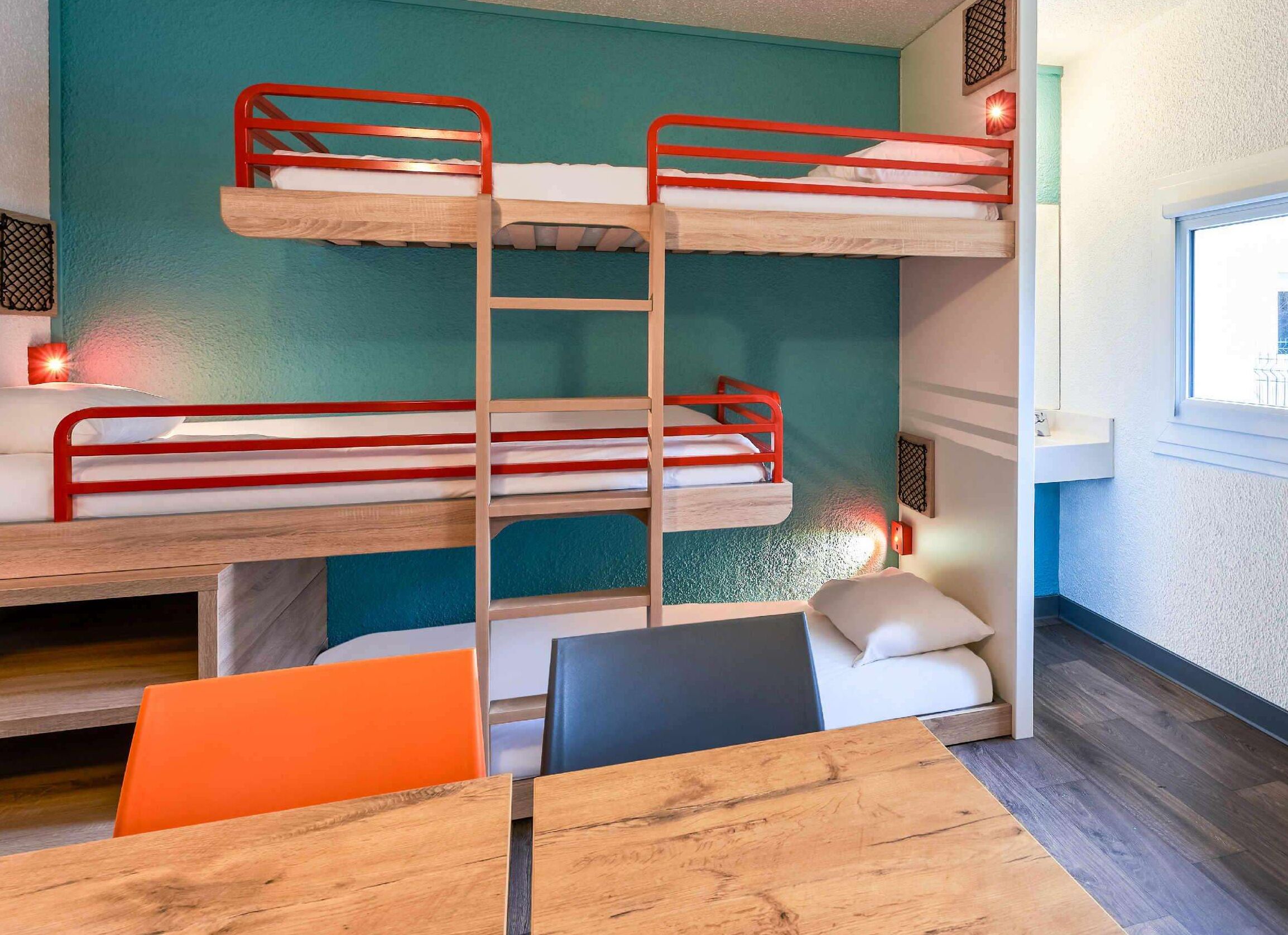 Habitación con literas, una mesa de madera y sillas naranjas.