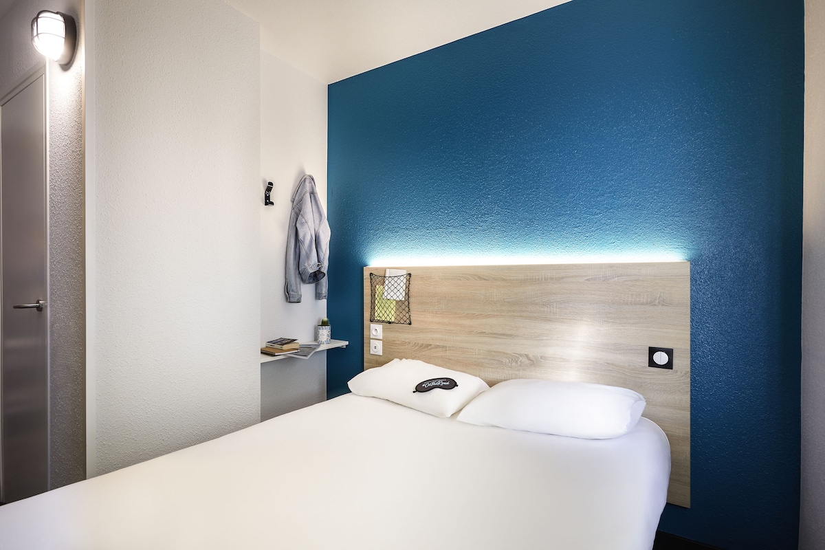Une chambre d’hôtel moderne avec un lit blanc, une tête de lit en bois et un mur d’accent bleu.