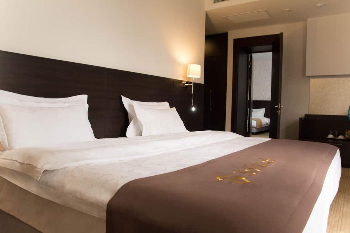 A hotel room with a large bed, a nightstand, a lamp, and a door leading to another room.
