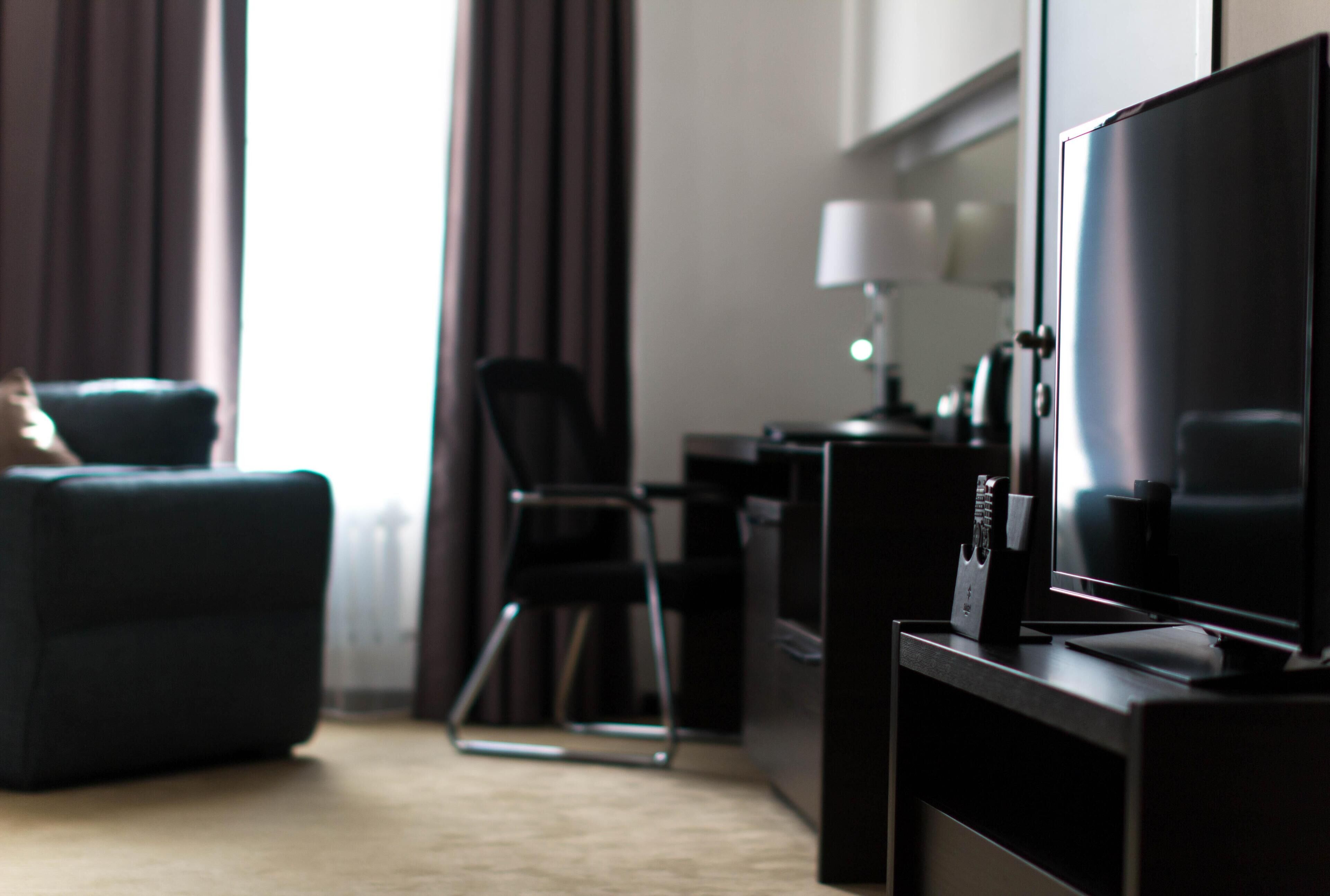 Una habitación de hotel moderna con una televisión de pantalla plana, un sofá, una silla y un escritorio con lámpara.