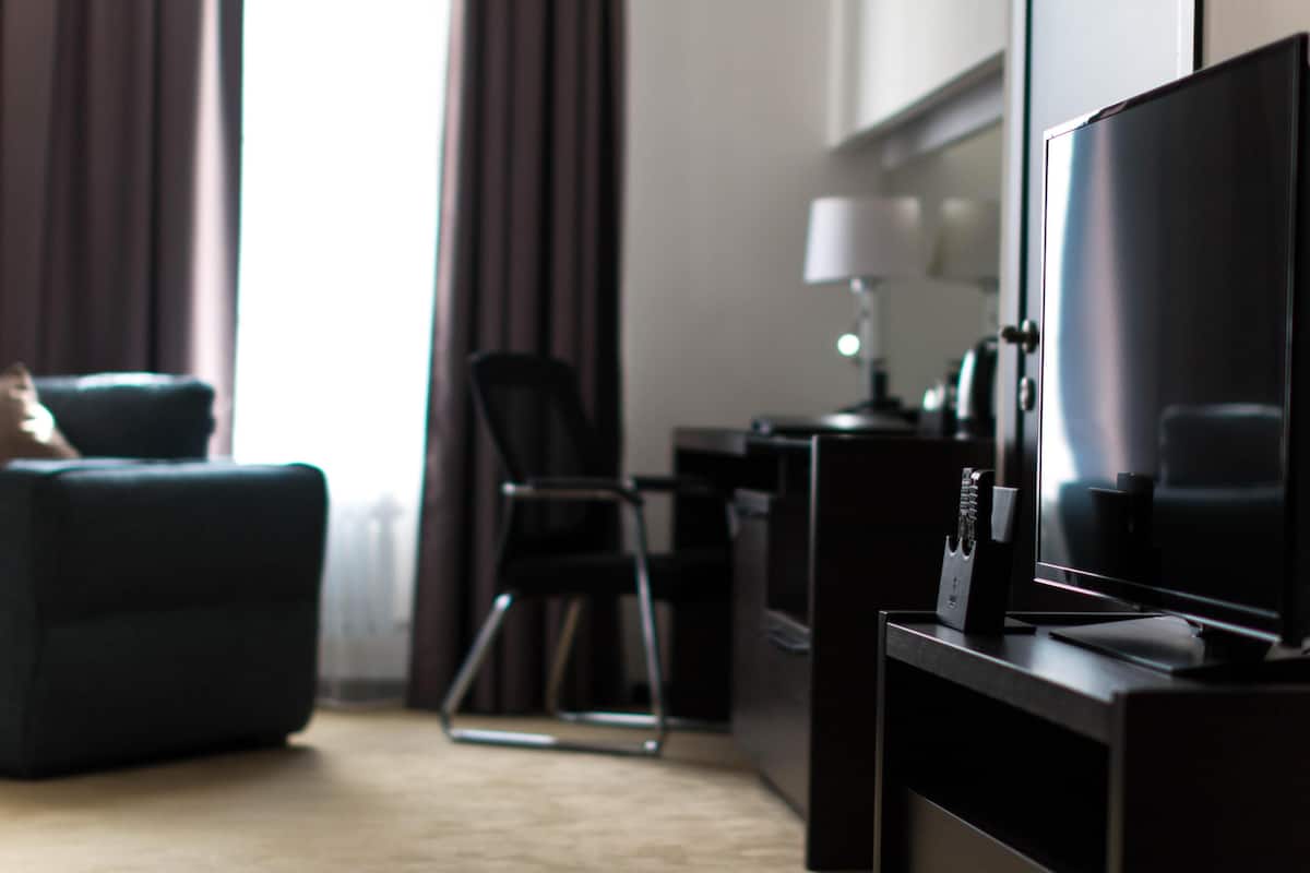 A modern hotel room with a flat-screen TV, a sofa, a chair, and a desk with a lamp.