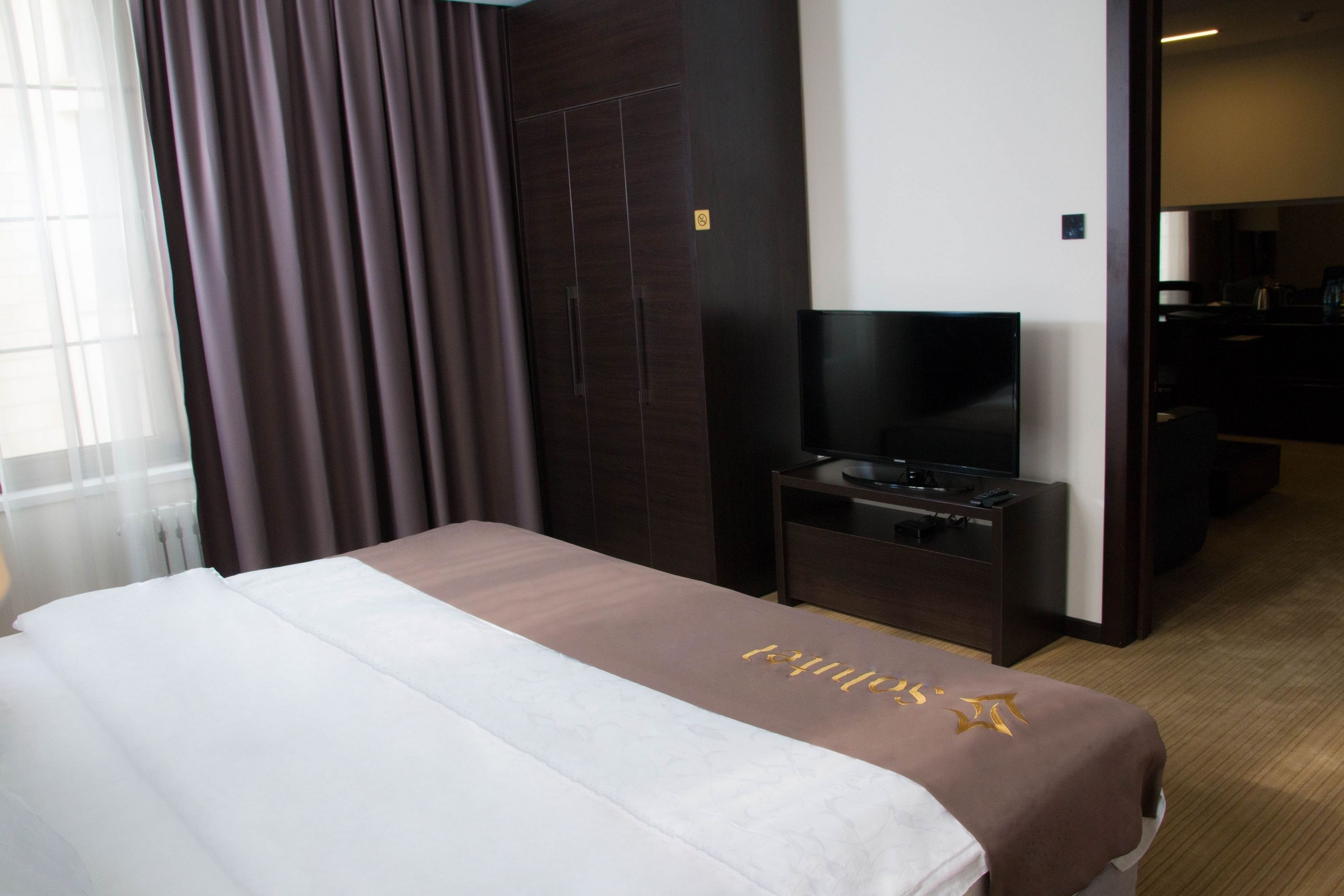 Une chambre d’hôtel avec un lit, un téléviseur posé sur un meuble, un bureau et une armoire.