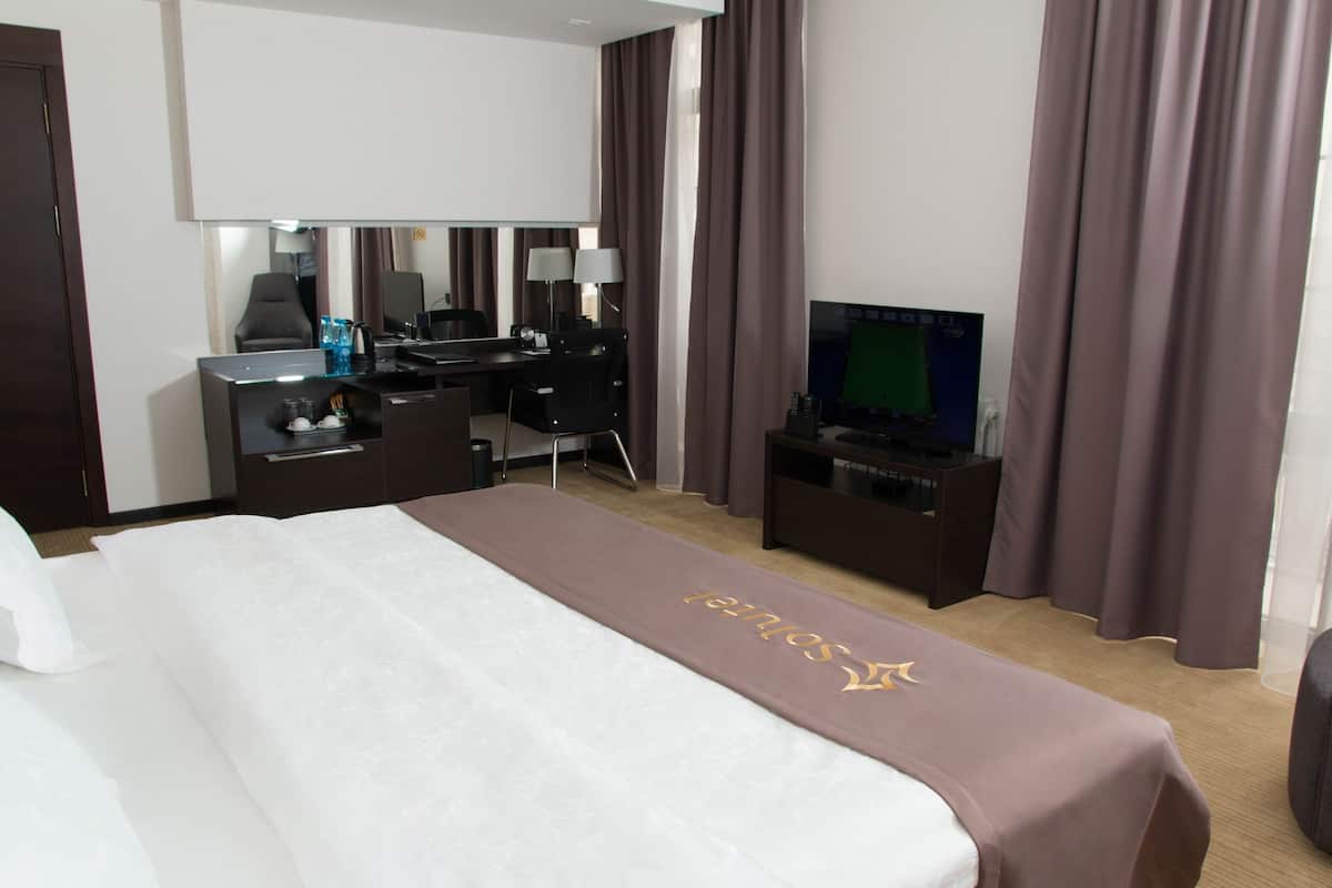 A hotel room with a bed, a desk, a television, and a large window with curtains.