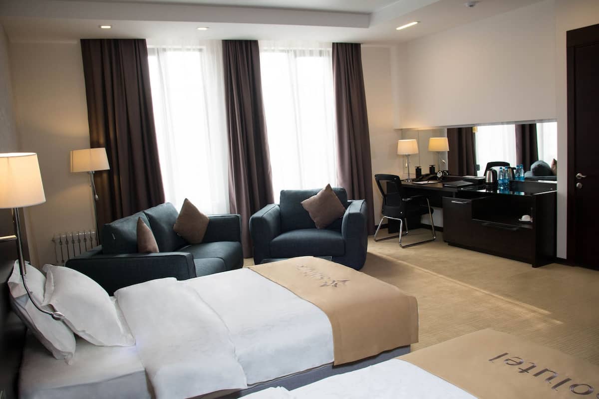 A hotel room with a bed, two armchairs, a desk, and a large mirror.