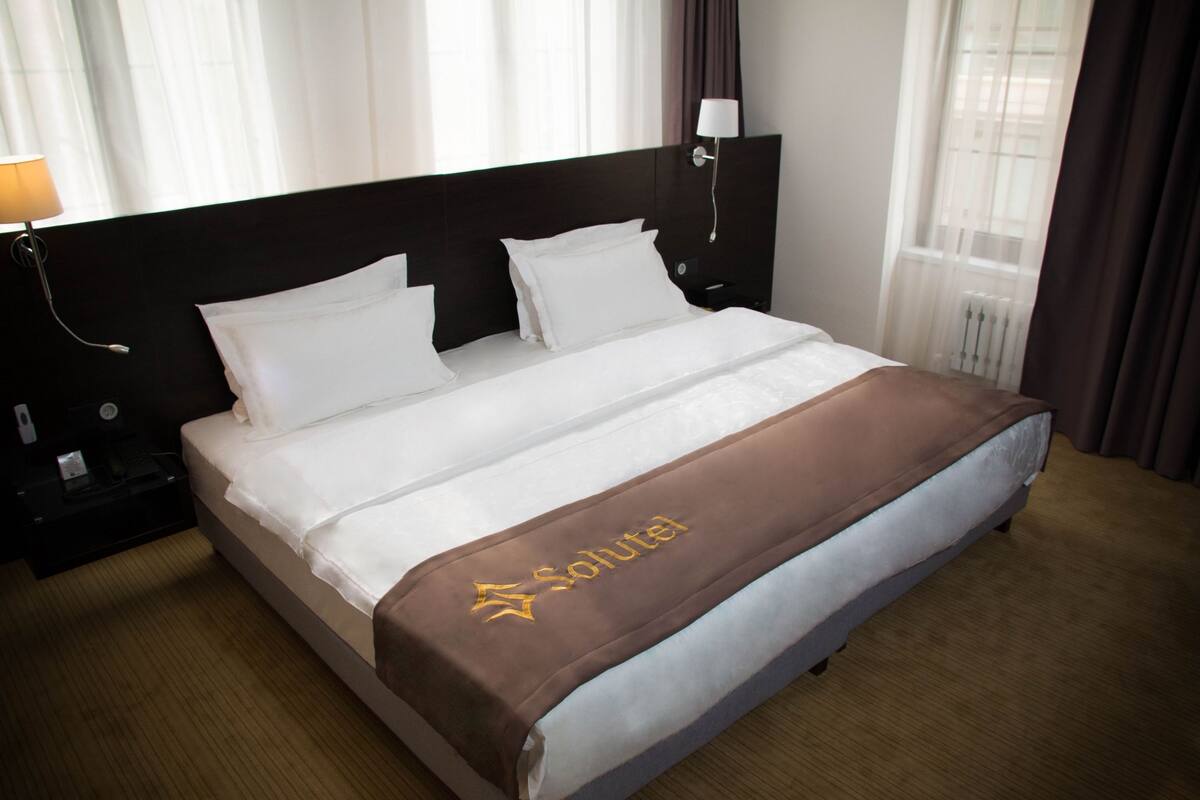 A hotel room with a bed, a nightstand, a lamp, and a window with curtains.