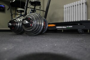 Un conjunto de pesas sobre el suelo, con una cinta de correr al fondo.