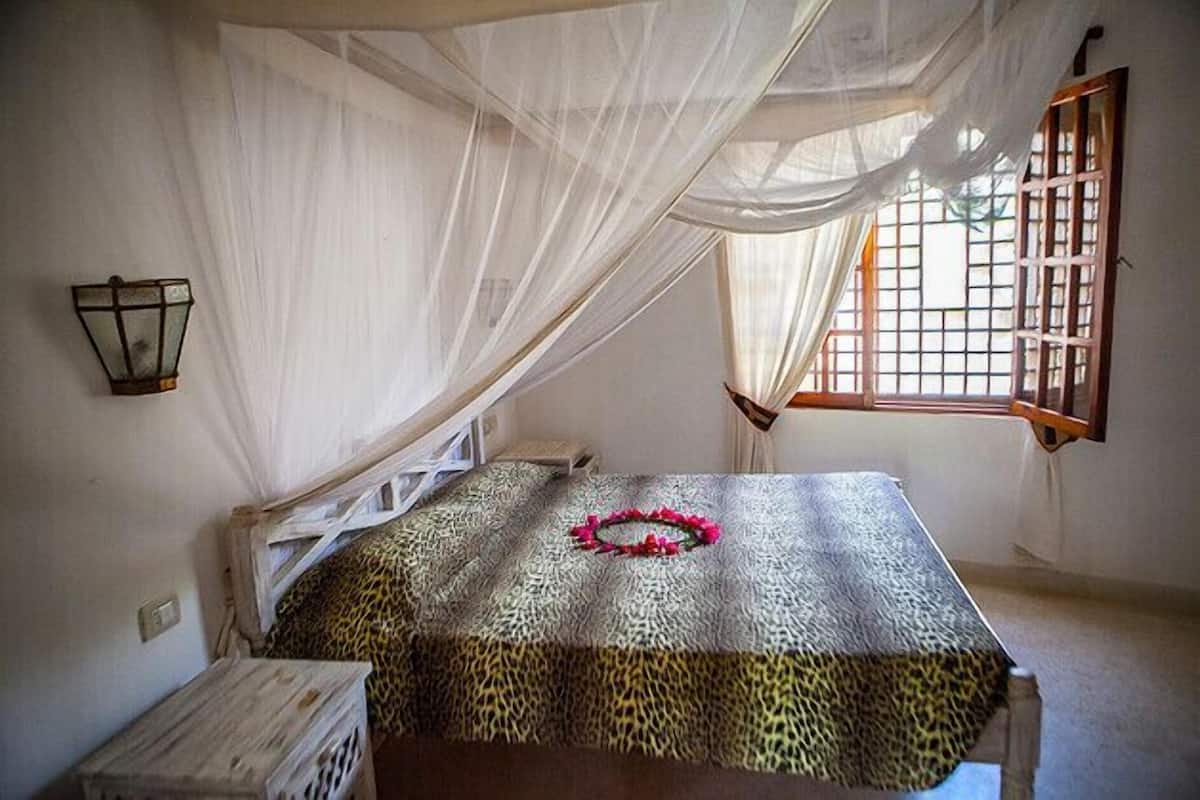 A room with a bed under a canopy, a window with bars, and a wall-mounted light fixture.
