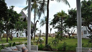 A covered outdoor seating area with white furniture, surrounded by lush greenery and palm trees. - Kola Beach Resort (Malindi)