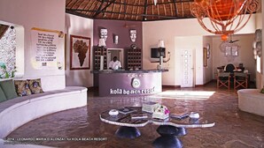 A reception area with a counter, a seating area with a round table, and a thatched roof ceiling. - Kola Beach Resort (Malindi)