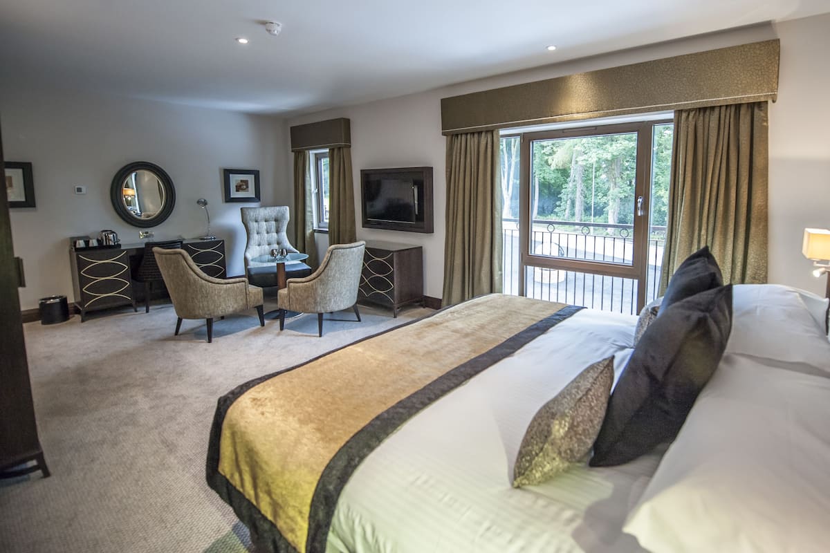 Une chambre d’hôtel avec un grand lit, un bureau avec une chaise, une télévision et un balcon donnant sur la verdure.