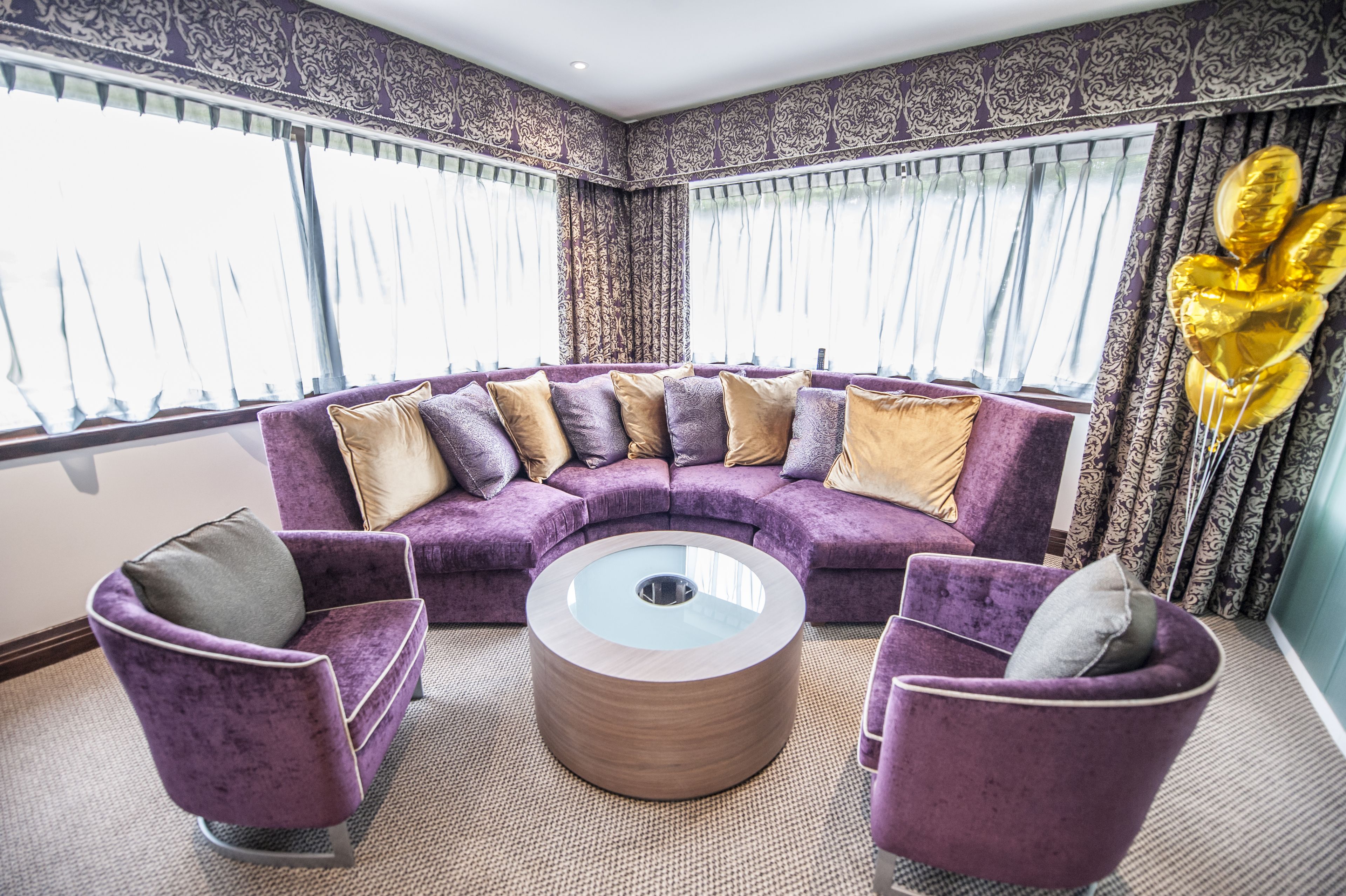 Sala de estar com canto, sofá seccional roxo, duas poltronas roxas e uma mesa de centro de vidro.