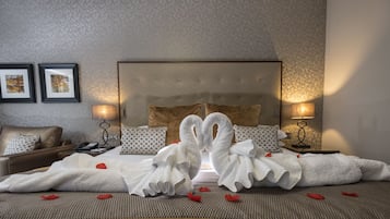 Habitación de hotel con una cama grande, dos lámparas de noche, un sillón de cuero marrón y dos cuadros en la pared.