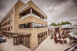 Un bâtiment à deux étages dont la façade porte l’inscription « Parklands Hotel ». On y trouve des espaces extérieurs aménagés avec des tables et des chaises, ainsi qu’une terrasse couverte.