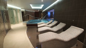 Un espace spa moderne doté d’un jacuzzi, de chaises longues et d’une douche séparée par des parois en verre.