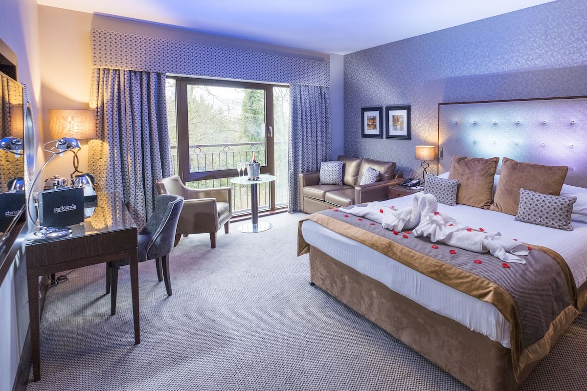 Une chambre d’hôtel avec un grand lit, un bureau, une chaise, un balcon et une vue sur les arbres.