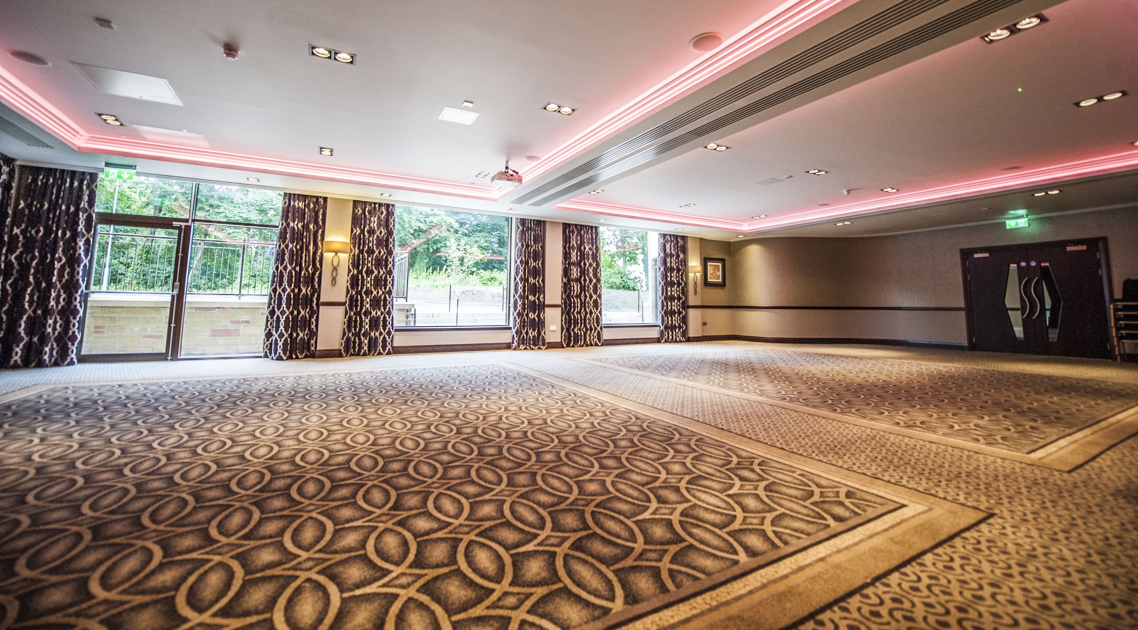 A spacious hotel lobby with patterned carpet, large windows, and a modern ceiling design.
