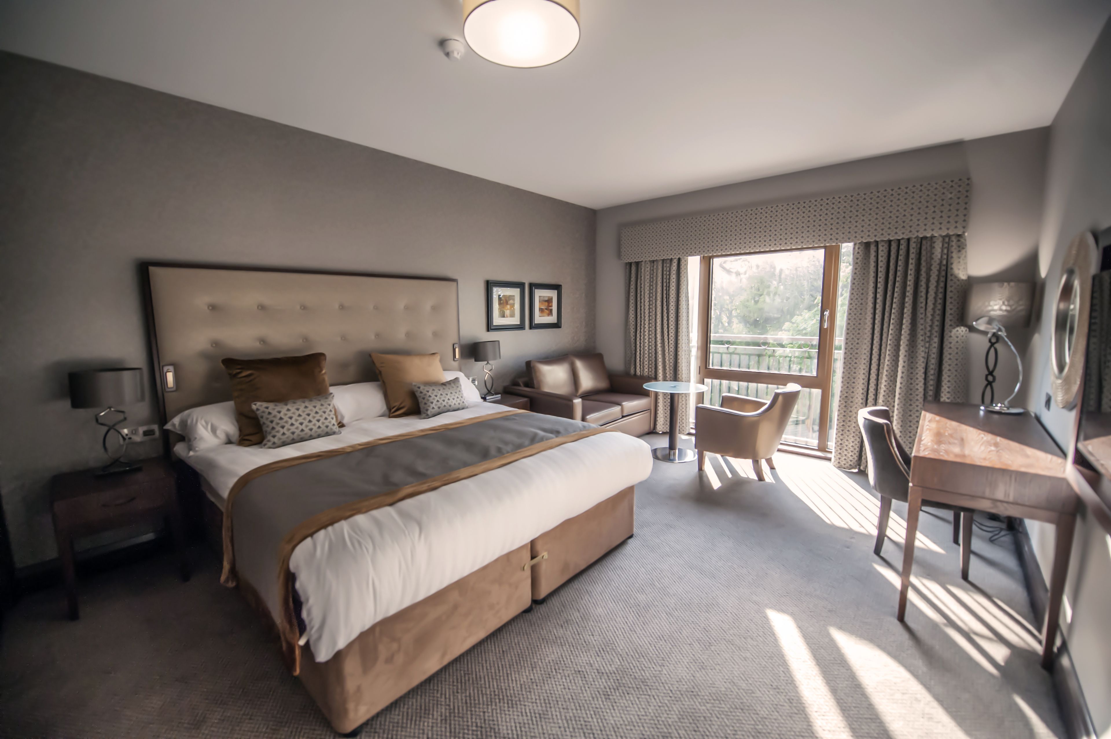 A hotel room with a large bed, a desk, a chair, and a view of the outdoors.