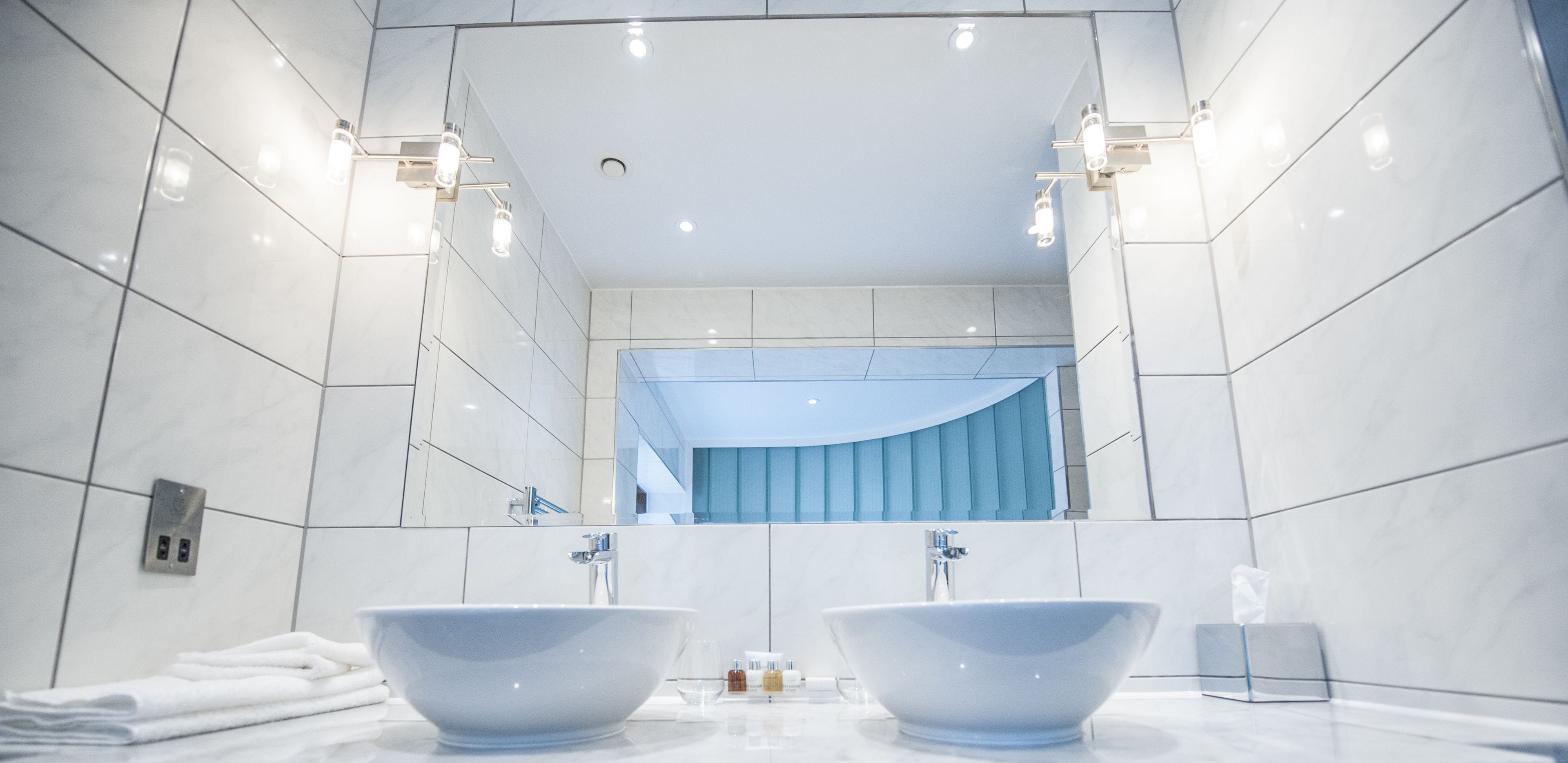 Une salle de bain moderne avec deux grands lavabos blancs, un miroir et un rideau bleu.