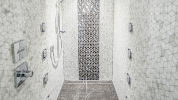 A modern shower with a geometric tile pattern, a central control panel, and a dark floor.