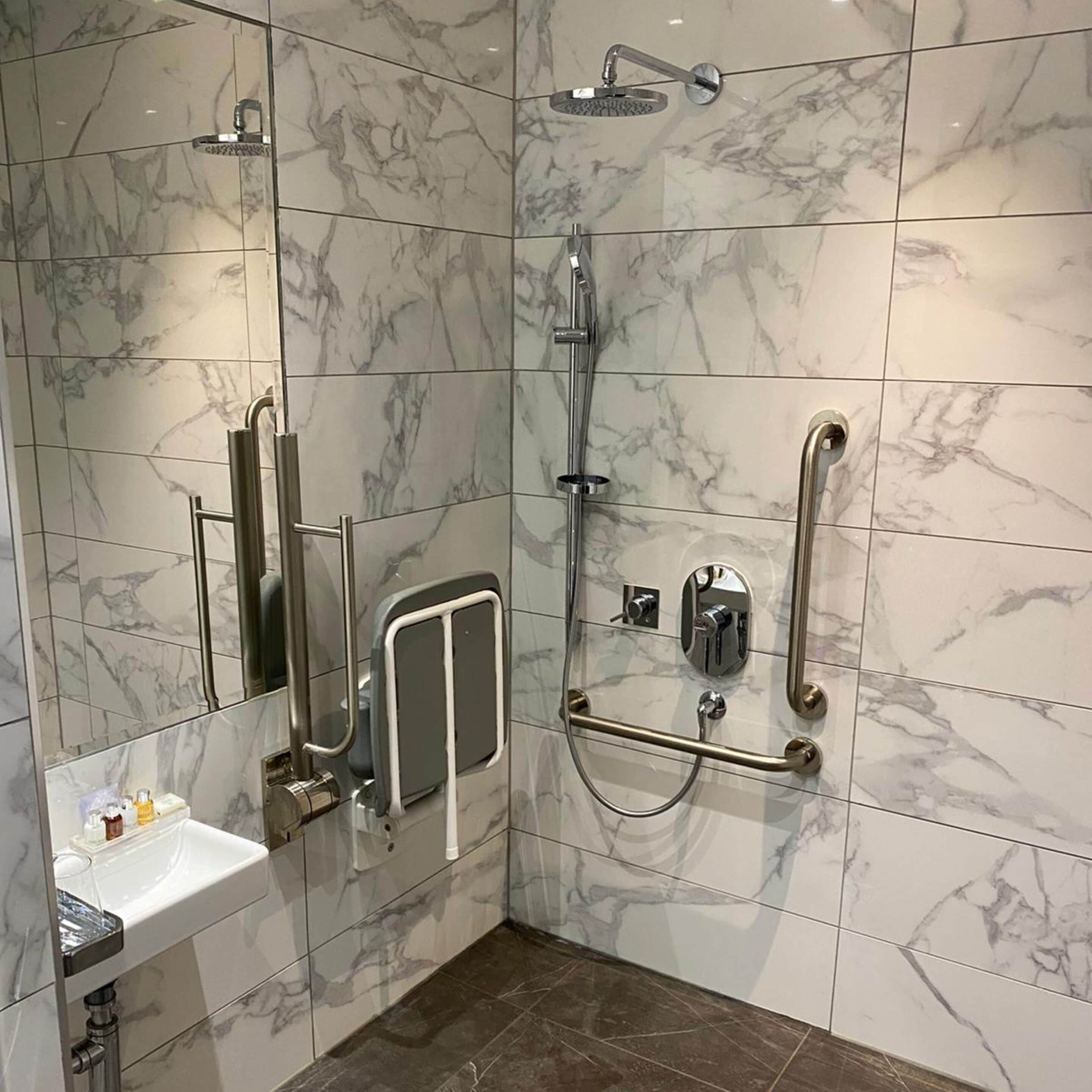 A modern bathroom with a walk-in shower, grab bars, and a white sink.