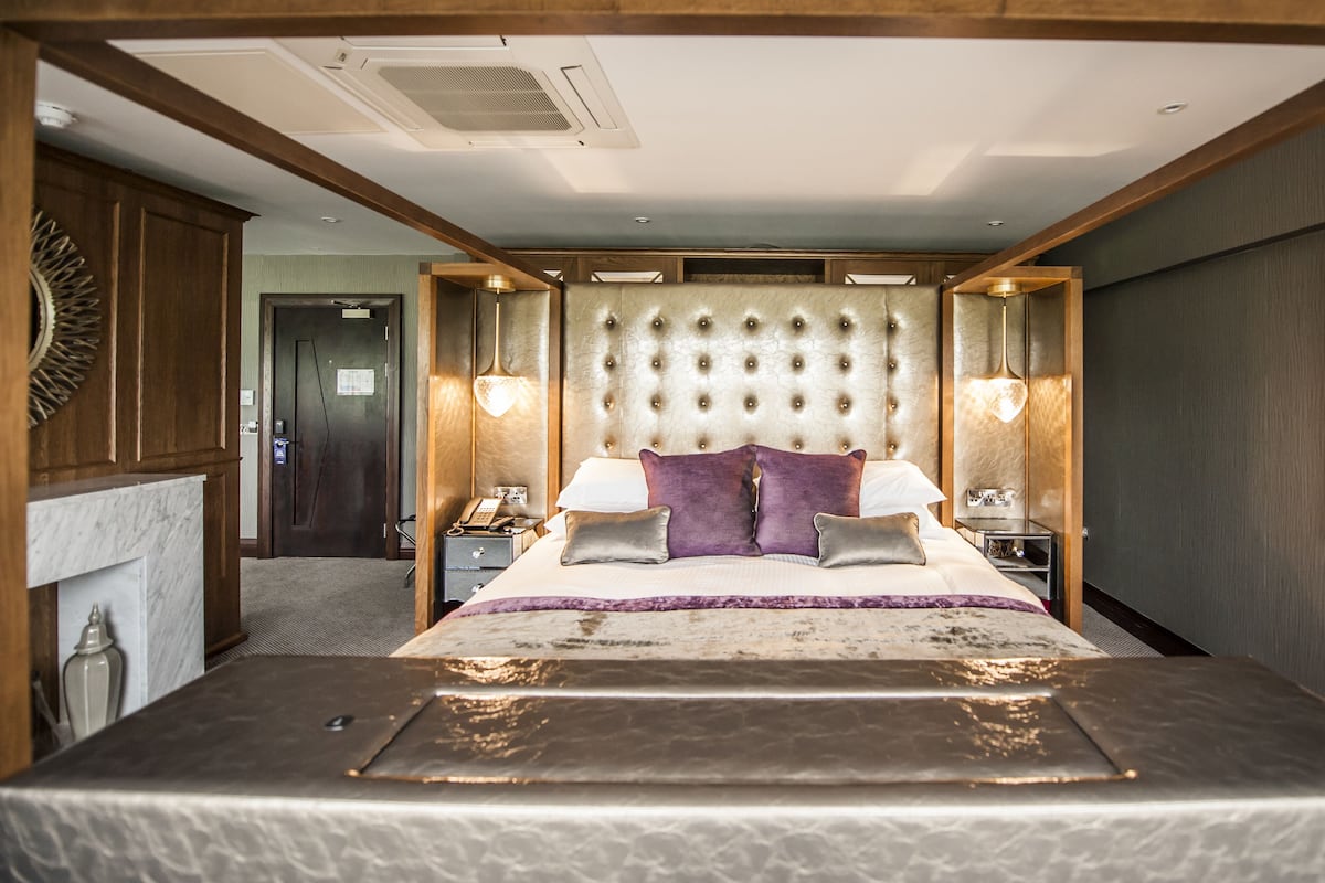 Une chambre spacieuse avec un grand lit, une tête de lit capitonnée, des lampes de chevet et une table de chevet.