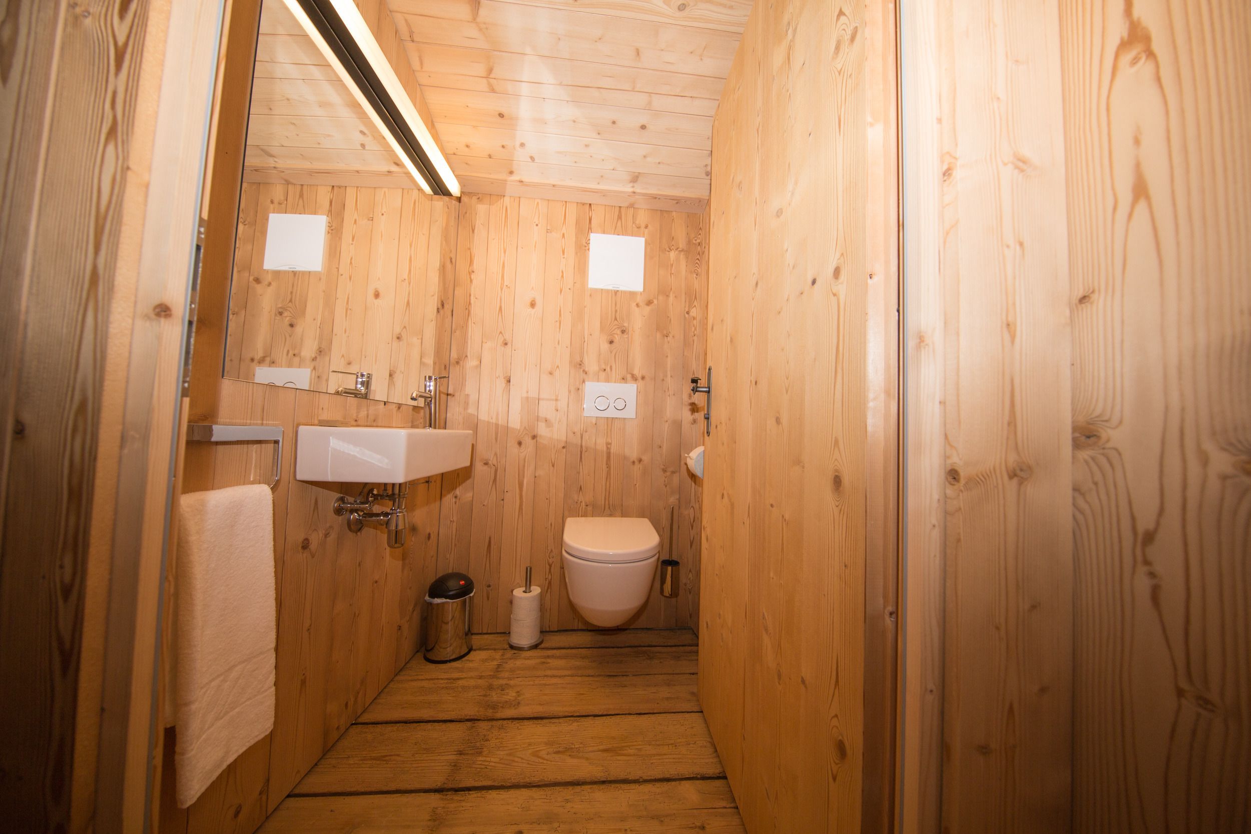 Un baño con paneles de madera, un lavamanos, un inodoro y un cubo de basura.
