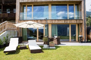 Un bâtiment moderne en bois, doté de grandes fenêtres en verre, d’un espace extérieur aménagé avec une table et des chaises, et d’une pelouse verdoyante.
