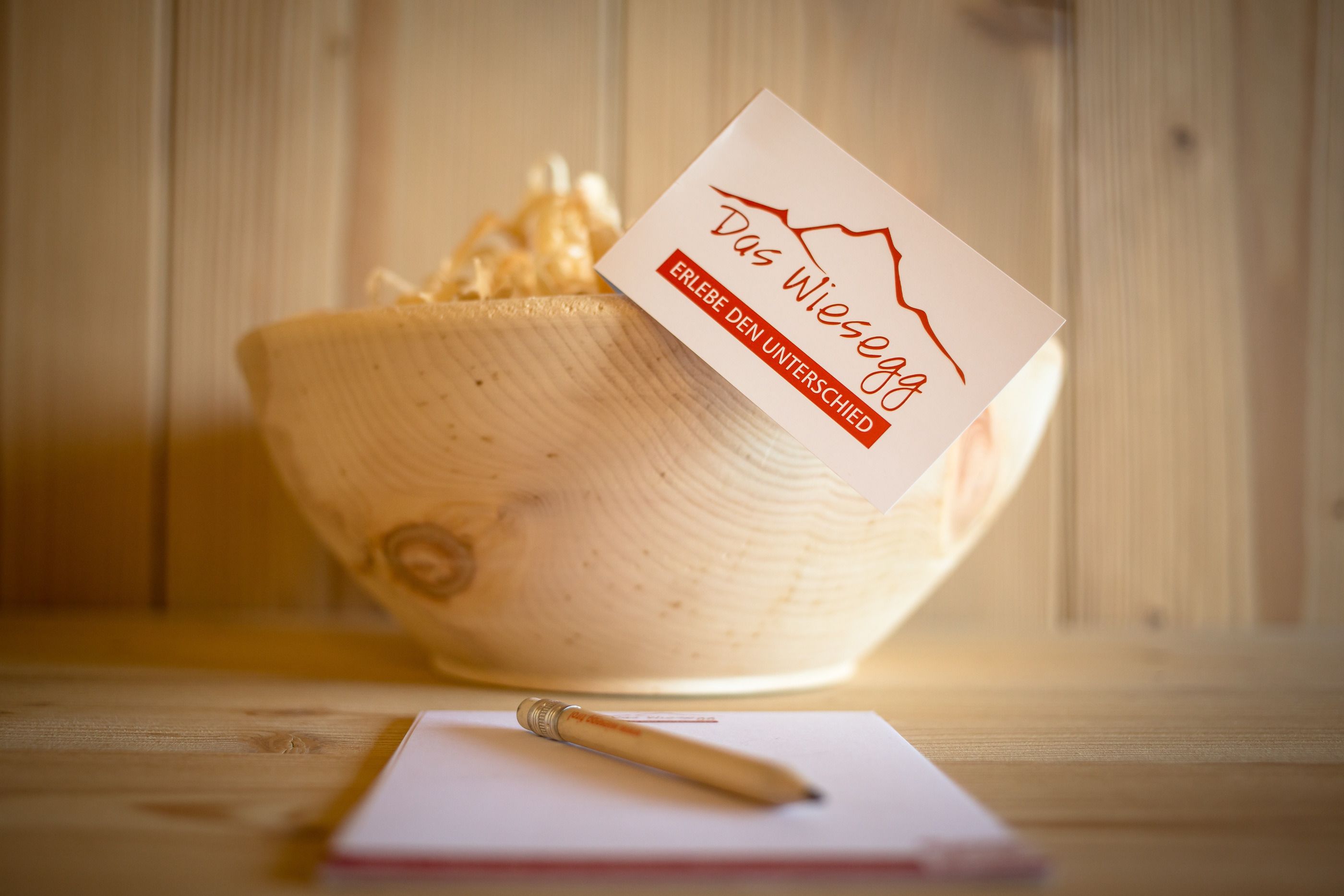 A wooden bowl with a card on it, a pen, and a notebook on a wooden surface.