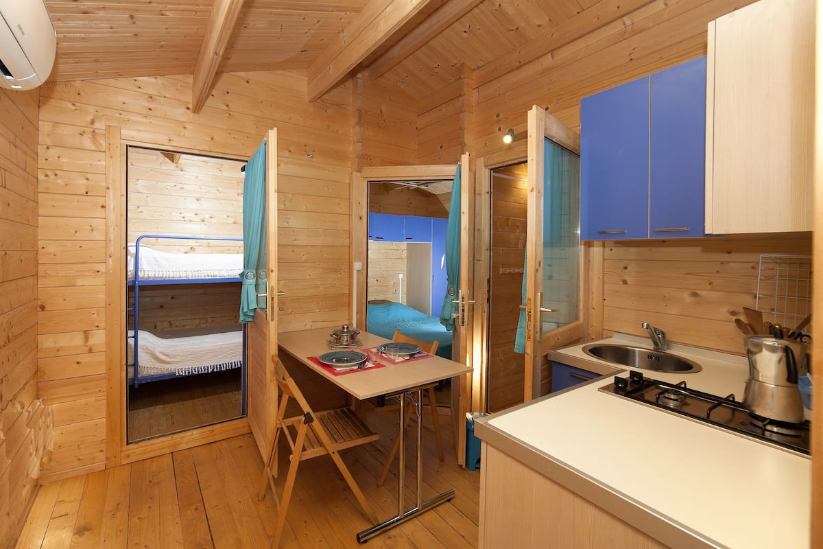 Une petite cabane en bois comprenant un lit superposé, une petite kitchenette et une salle de bain.