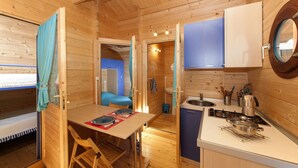 A compact wooden cabin with a dining area, a small kitchen with a stove, and a sleeping area with a bunk bed. - Camping Merendella (San-Nicolao)