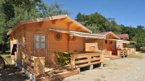 A wooden cabin with a porch, a table, and a chair. - Camping Merendella (San-Nicolao)