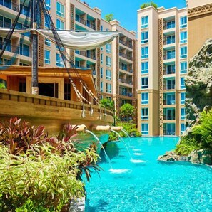 A swimming pool with a ship-shaped structure, surrounded by lush greenery and a multi-story building in the background. - Atlantis Condo and Water Park Pattaya by the Sea (Pattaya)