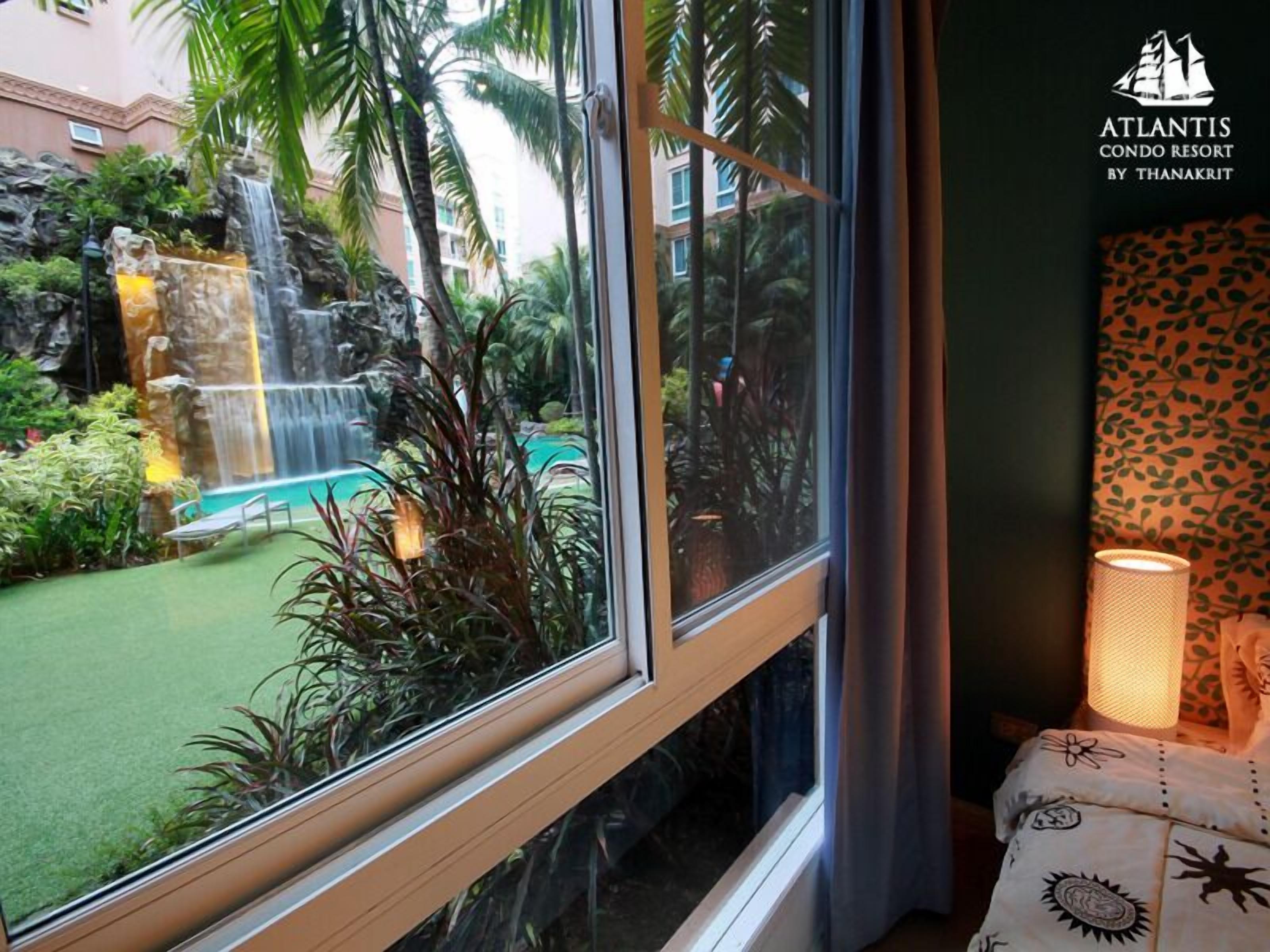 A window view of a resort's outdoor area with a waterfall, pool, and lush greenery.