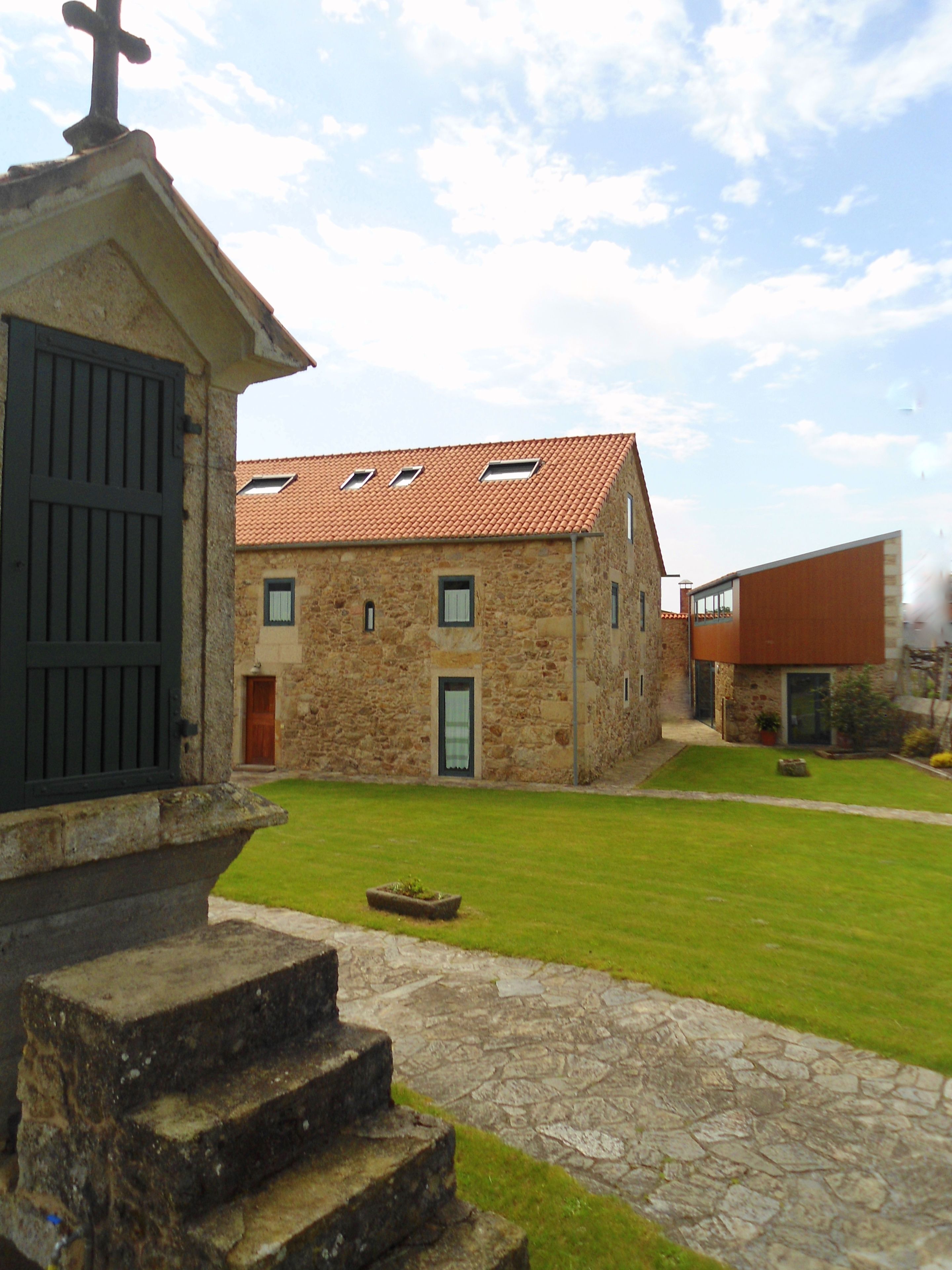 A stone building with a tiled roof, a small garden, and a staircase leading to a door.