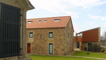 A stone building with a tiled roof, a small garden, and a staircase leading to a door.